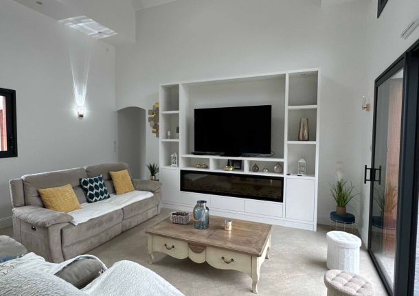Salon lumineux avec meuble TV blanc sur mesure, intégrant des rangements et une cheminée électrique, accompagné de canapés beiges, une table basse en bois et des éléments de décoration élégants.